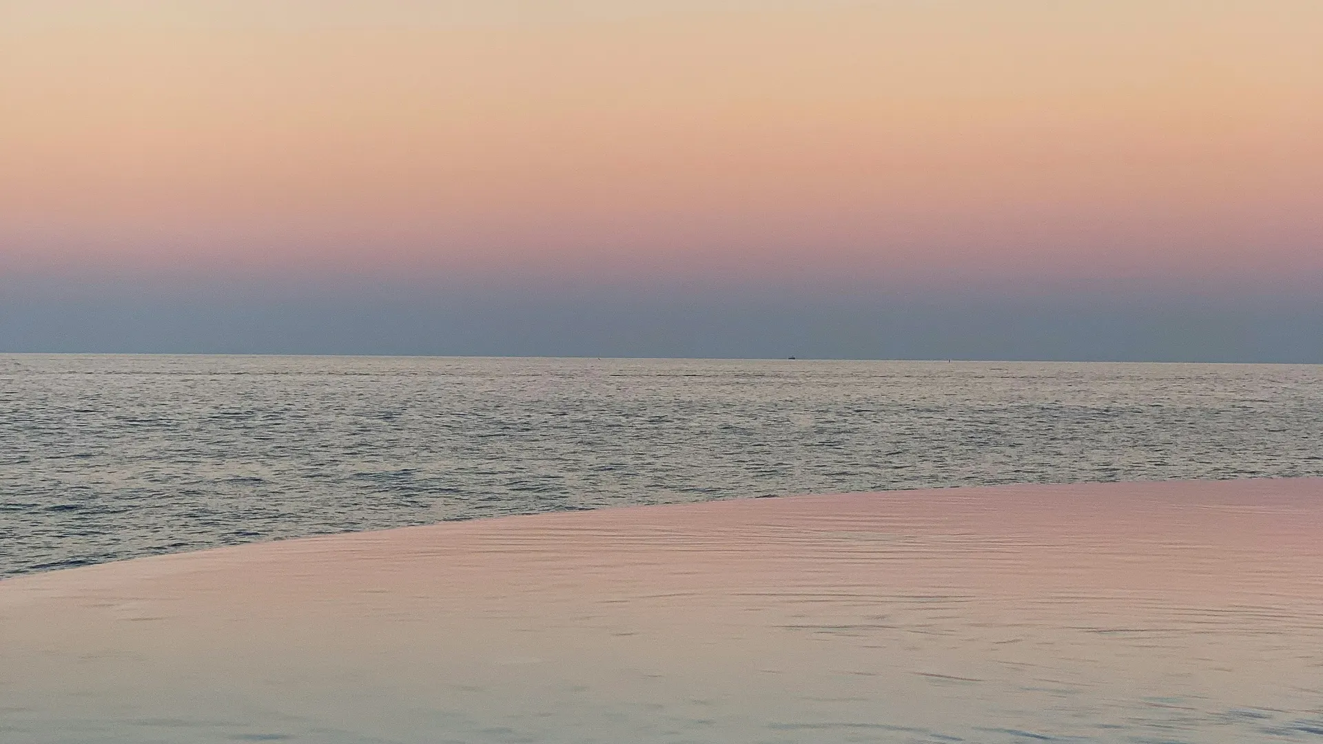 Borde de una piscina infinita que se funde con el mar al atardecer